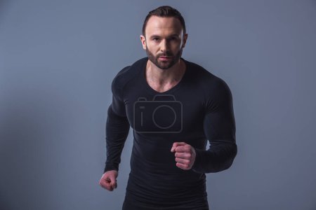 Foto de Retrato de hombre musculoso guapo en jersey negro ajustado mirando a la cámara, sobre fondo gris - Imagen libre de derechos