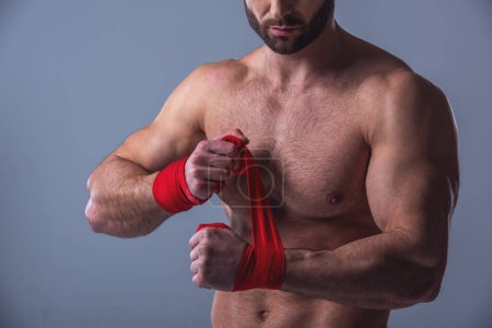Téléchargez les photos : Image recadrée d'un bel homme musclé avec torse nu bandant les mains avant la boxe, sur fond gris - en image libre de droit