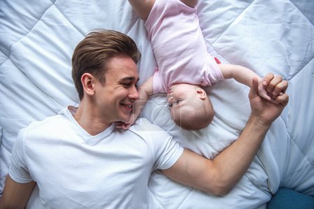 Photo for Top view of handsome young dad and his cute baby looking at each other while lying on bed - Royalty Free Image