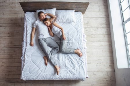 Téléchargez les photos : Vue du dessus de beau jeune couple embrassant tout en dormant ensemble dans le lit à la maison - en image libre de droit