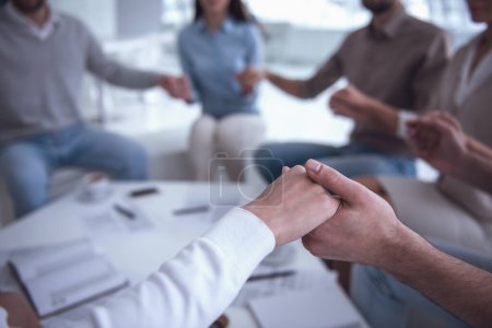 Téléchargez les photos : Équipe d'affaires tient la main ensemble tout en étant assis en cercle dans le bureau - en image libre de droit