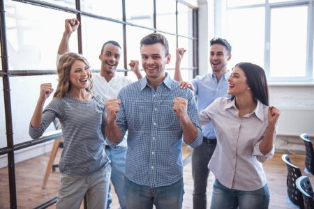 Photo for Successful business team is raising hands in fists and smiling while standing in office - Royalty Free Image