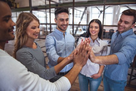 Photo for Successful business team is giving high five and smiling while standing in office - Royalty Free Image