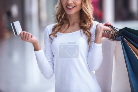 Foto de Imagen recortada de una hermosa chica con bolsas de compras sosteniendo una tarjeta de crédito y sonriendo mientras hace compras en el centro comercial - Imagen libre de derechos