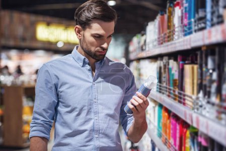 Photo for Handsome man is choosing cosmetics while doing shopping at the supermarket - Royalty Free Image