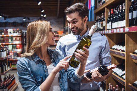 Téléchargez les photos : Beau jeune couple parle et sourit tout en choisissant du vin au supermarché - en image libre de droit