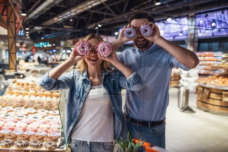 Téléchargez les photos : Beau couple tient des beignets et sourit tout en faisant du shopping au supermarché - en image libre de droit