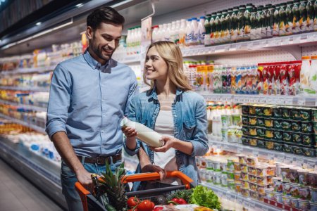 Foto de Hermosa pareja está hablando y sonriendo mientras hace compras en el supermercado - Imagen libre de derechos