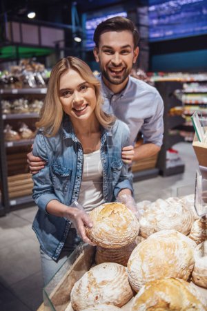 Téléchargez les photos : Beau jeune couple choisit la cuisson et le sourire tout en faisant du shopping au supermarché - en image libre de droit