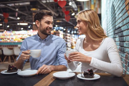 Téléchargez les photos : Beau jeune couple boit du café, parle et sourit tout en se reposant dans le centre commercial - en image libre de droit