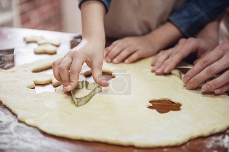Téléchargez les photos : Image recadrée de la petite fille et de sa mère dans des tabliers préparant des biscuits à l'aide de coupe-biscuits dans la cuisine - en image libre de droit