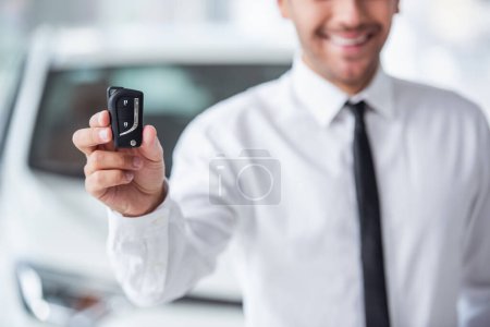 Photo for Cropped image of handsome businessman in suit holding key and smiling while standing in car dealership - Royalty Free Image