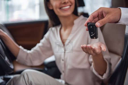 Foto de Hermosa joven mujer está recibiendo la llave y sonriendo mientras está sentado en un coche nuevo en la concesionaria - Imagen libre de derechos