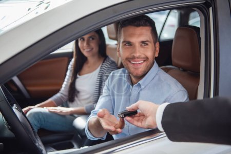 Foto de Visitando concesionario de coches. Hermosa pareja está recibiendo una llave del coche y sonriendo mientras está sentado en su nuevo coche - Imagen libre de derechos
