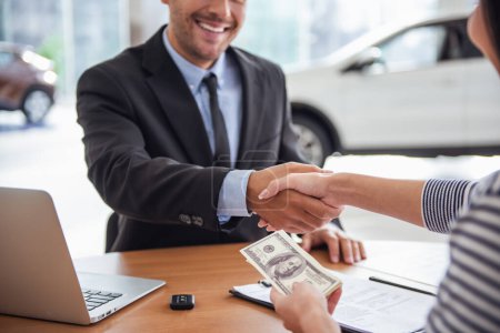Foto de Visitando concesionario de coches. Guapo gerente de ventas está estrechando la mano con un cliente y sonriendo - Imagen libre de derechos