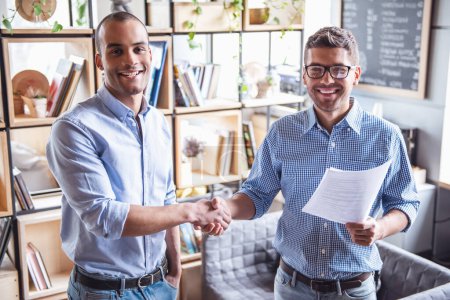 Photo for Successful partnership. Handsome businessmen are shaking hands and smiling while standing in office - Royalty Free Image