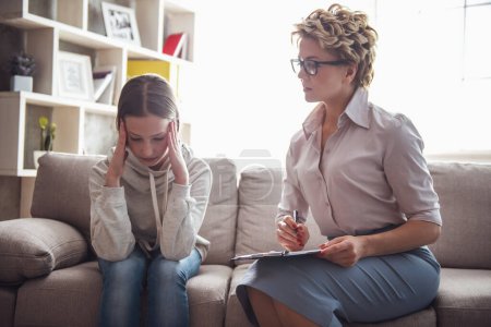 Teenager-Mädchen beim Psychotherapeuten. beide sitzen auf dem Sofa im Büro, Arzt macht Notizen