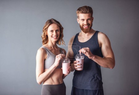 Foto de Hermosos jóvenes deportistas están celebrando cócteles nutritivos, mirando a la cámara y sonriendo, sobre un fondo gris - Imagen libre de derechos