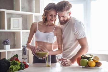 Foto de Hermosa pareja joven está hablando y sonriendo mientras cocina alimentos saludables en la cocina en casa - Imagen libre de derechos