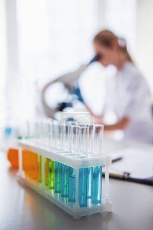 Photo for At the laboratory. Test tube with substances in the foreground, doctor is using a microscope in the background - Royalty Free Image
