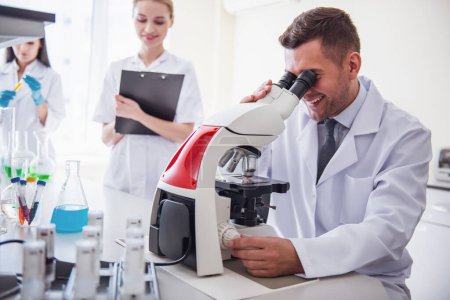 Photo for Handsome medical doctor is using a microscope and smiling while working at the lab - Royalty Free Image