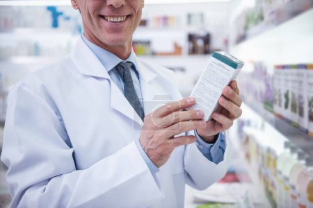 Photo for Cropped image of handsome pharmacist holding a medication and smiling while standing in pharmacy - Royalty Free Image