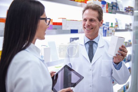 Foto de Hermosos farmacéuticos están discutiendo medicamentos, usando una tableta digital y sonriendo mientras trabajan en la farmacia - Imagen libre de derechos