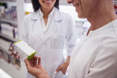 Téléchargez les photos : Belle jeune pharmacienne suggère un médicament à un client à la pharmacie et souriant - en image libre de droit