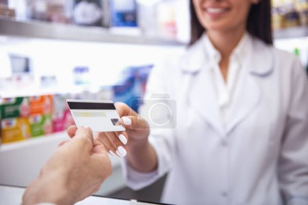 Photo for At the pharmacy. Cropped image of young female pharmacist taking a credit card from a client while working at the cash desk - Royalty Free Image