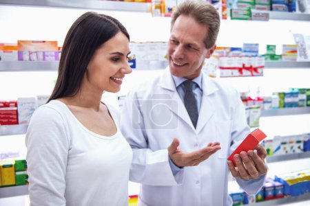 Téléchargez les photos : Beau pharmacien offre un médicament à une belle jeune cliente à la pharmacie, les deux sourient - en image libre de droit