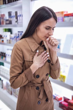 Foto de Hermosa mujer joven está tosiendo mientras busca un medicamento en la farmacia - Imagen libre de derechos