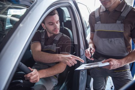 Téléchargez les photos : Beau jeune mécanicien automobile en uniforme prennent des notes tout en examinant la voiture en service automobile - en image libre de droit