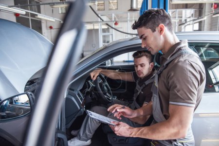Photo for Handsome young auto mechanics in uniform are making notes while examining car in auto service - Royalty Free Image
