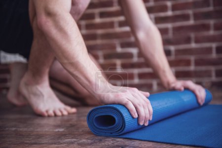 Téléchargez les photos : Cropped image de gars roulant un tapis de yoga après l'entraînement - en image libre de droit