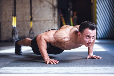 Photo for Handsome young muscular sportsman is doing push-ups while working out in gym - Royalty Free Image
