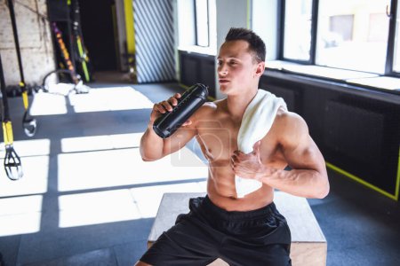 Téléchargez les photos : Beau jeune sportif musclé boit de l'eau tout en se reposant après l'entraînement dans la salle de gym - en image libre de droit