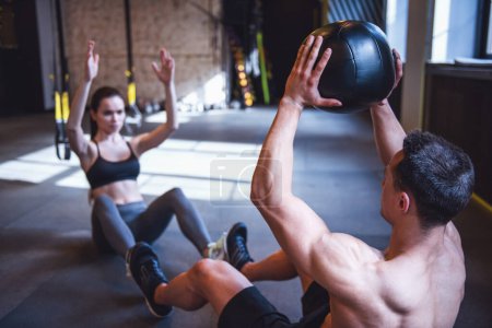 Photo for Beautiful young sports couple is working out with medicine ball in gym - Royalty Free Image