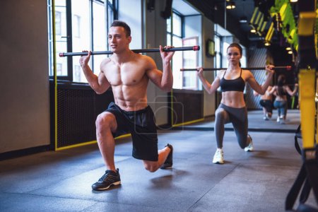 Photo for Beautiful young sports people are doing lunges with barbell while working out in gym - Royalty Free Image