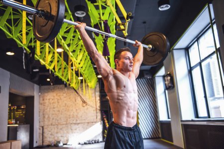 Foto de Guapo joven deportista muscular está haciendo ejercicio con barra de pesas en el gimnasio - Imagen libre de derechos