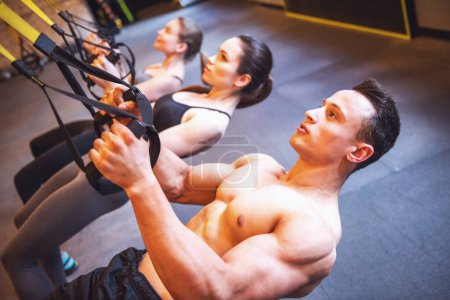 Photo for Beautiful young sports people are working out with TRX in gym - Royalty Free Image