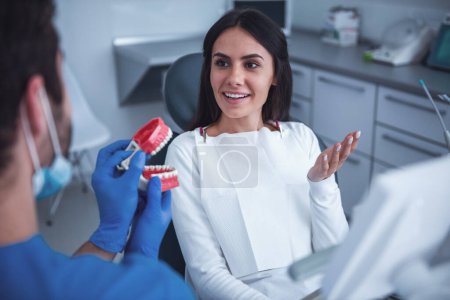 Foto de Hermosa mujer está sentada en la silla del dentista y escuchando al médico - Imagen libre de derechos