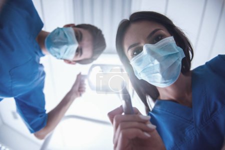 Téléchargez les photos : Vue du bas des dentistes dans le masque chirurgical tenant des outils et regardant la caméra - en image libre de droit