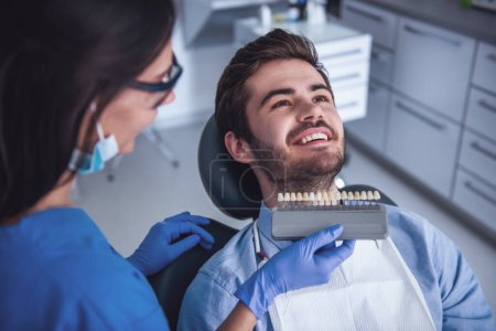 Foto de Un joven guapo está sentado en la silla del dentista mientras el médico le examina los dientes. - Imagen libre de derechos