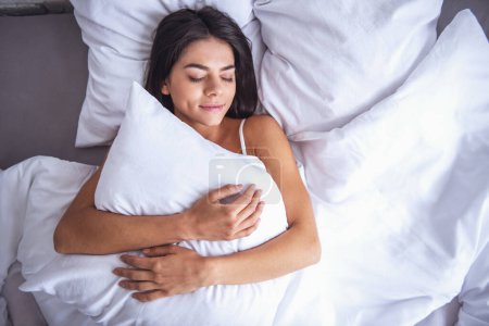 Téléchargez les photos : Jeune belle fille dort dans le lit étreignant l'oreiller vue dessus - en image libre de droit
