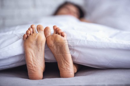 Téléchargez les photos : Beaux pieds de femme endormie sous la couverture sur son lit. Chambre sur fond
. - en image libre de droit