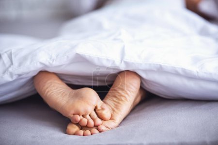 Téléchargez les photos : Beaux pieds de femme endormie sous la couverture sur son lit. Chambre sur fond
. - en image libre de droit