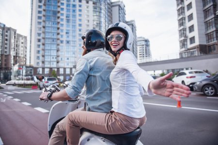 Téléchargez les photos : Beau jeune couple en lunettes de soleil et casques sourit tout en montant un scooter - en image libre de droit