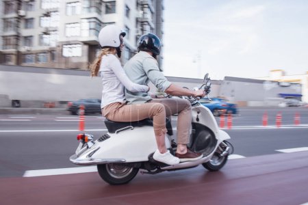 Photo for Side view of beautiful young couple in helmets riding a scooter - Royalty Free Image