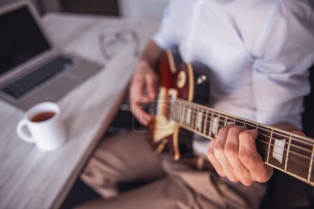 Téléchargez les photos : Image recadrée d'un jeune homme d'affaires jouant de la guitare dans son bureau pendant la pause - en image libre de droit