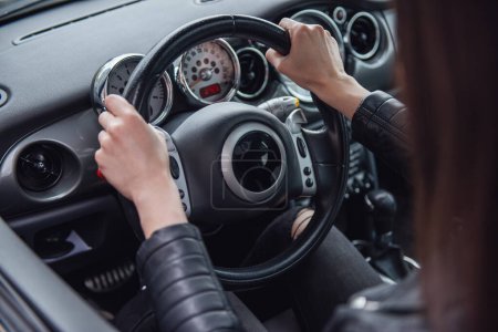 Photo for Cropped image of girl in leather jacket driving a car, hands on steering wheel - Royalty Free Image